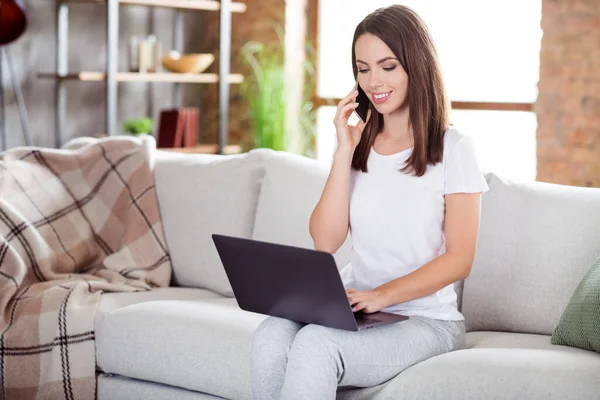 Foto di attraente giovane donna positiva tenere telefono parlare telefono guardare computer portatile all'interno della casa a casa — Foto Stock