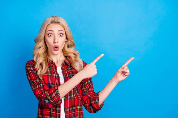 Foto von charmant beeindruckt junge Dame tragen kariertes Hemd zeigt mit den Fingern leeren Raum große Augen isoliert blaue Farbe Hintergrund — Stockfoto