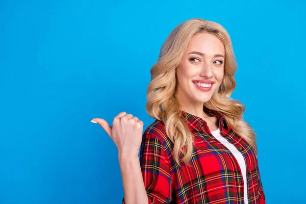 Photo of cute adorable young woman dressed checkered shirt smiling looking pointing thumb up empty space isolated blue color background — Stock Photo, Image