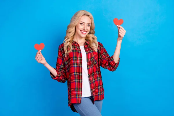 Foto de uma jovem mulher muito brilhante vestida camisa xadrez sorrindo segurando dois corações vermelhos isolado fundo de cor azul — Fotografia de Stock