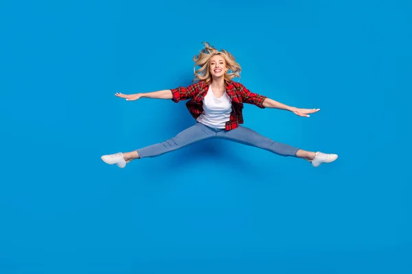 Foto von charmanten hübschen jungen Dame tragen kariertes Hemd lächelnd springen hohe Beine Hände Arme Seiten isoliert blaue Farbe Hintergrund — Stockfoto