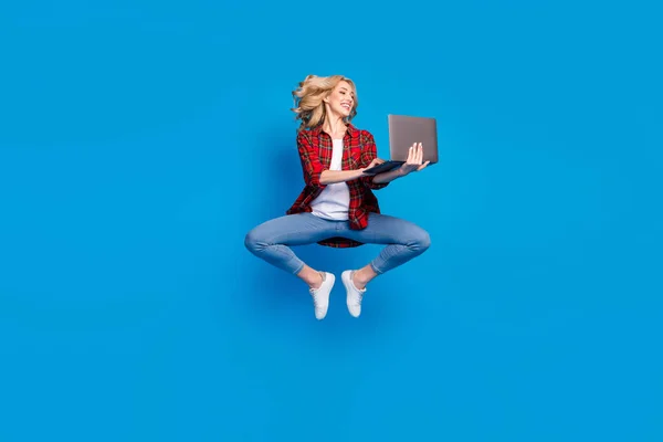 Foto de mulher muito adorável jovem vestido camisa quadriculada saltando alta digitação dispositivo moderno sorrindo isolado fundo cor azul — Fotografia de Stock