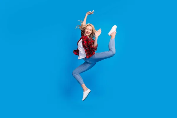 Çekici, parlak, genç bir kadının kareli gömlekli, atlayan, jimnastik yapan izole edilmiş mavi arka plan gülümseyen fotoğrafı. — Stok fotoğraf