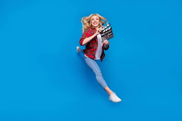 Foto di funky dolce giovane signora indossare camicia scozzese sorridente gobba alta tenendo clapperboard isolato sfondo di colore blu — Foto Stock