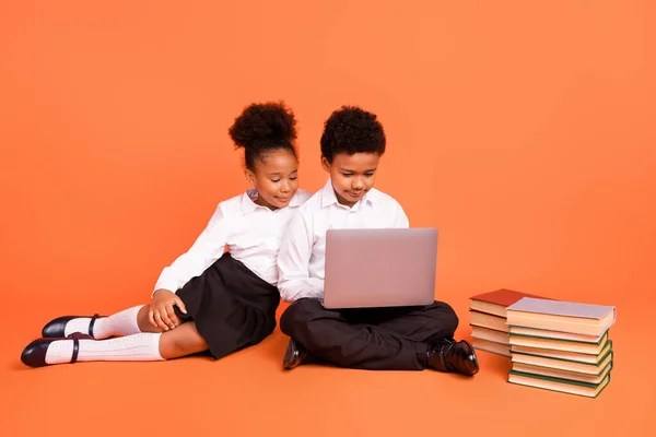 Volledige grootte foto van twee jonge afro school kinderen klasgenoten maken huiswerk computer geïsoleerd over oranje kleur achtergrond — Stockfoto