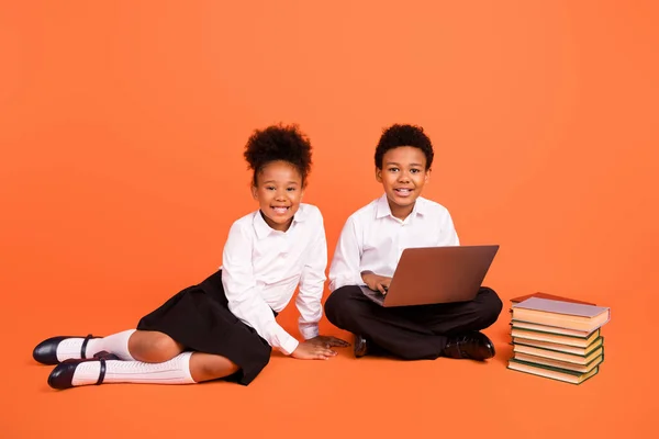 两个年轻的非洲裔学童学习在线笔记本电脑的全长照片，他们被橙色背景隔离 — 图库照片