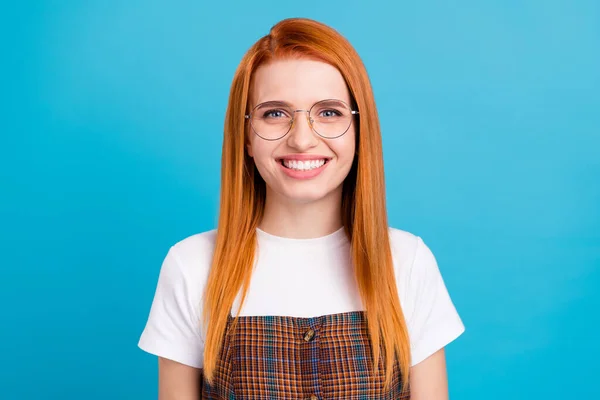 Foto av ganska charmiga orange hår dam bära rutig övergripande glasögon ler isolerad blå färg bakgrund — Stockfoto