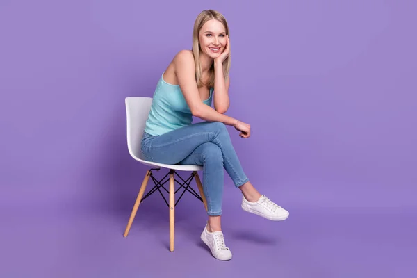 Full size foto van coole blonde millennial dame zitten dragen teal top jeans sneakers geïsoleerd op violette kleur achtergrond — Stockfoto