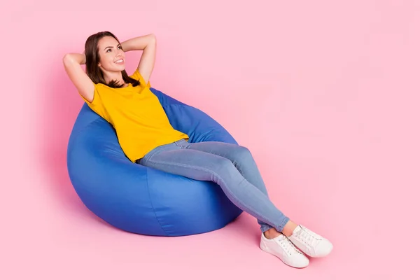Photo of pretty charming lady wear yellow t-shirt sitting beanbag arms behind head looking empty space isolated pink color background — Stock Photo, Image