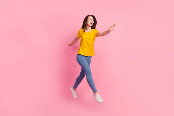 Full size foto di funky bruna capelli giovane signora salto indossare giallo t-shirt jeans isolato su sfondo rosa — Foto Stock