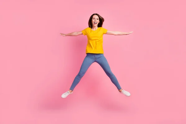 Foto de la afortunada adorable joven vestida con camiseta amarilla saltando alto como una estrella aislada de color rosa de fondo —  Fotos de Stock