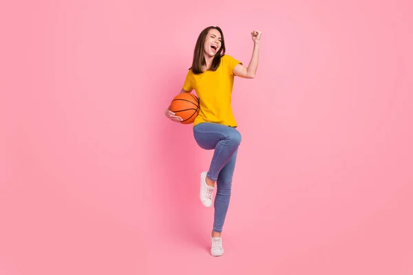 Foto di adorabile fortunata giovane donna vestita di giallo t-shirt in aumento pugno tenendo basket palla isolato colore rosa sfondo — Foto Stock