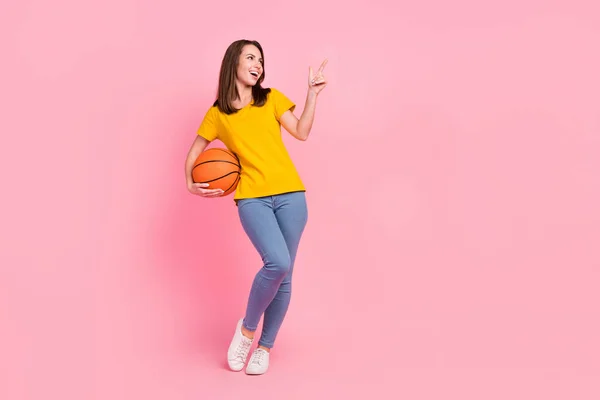 Full size foto di fresco bruna capelli giovane signora punto vuoto spazio tenere palla usura giallo t-shirt jeans isolato su sfondo rosa — Foto Stock