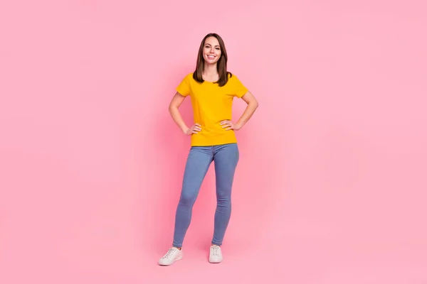 Foto de tamaño completo de buen cabello morena milenaria dama de pie usar pantalones vaqueros camiseta amarilla aislados en el fondo de color rosa — Foto de Stock