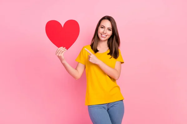 Foto de impressionado doce jovem mulher vestida amarelo t-shirt apontando dedo vermelho coração isolado cor de rosa fundo — Fotografia de Stock