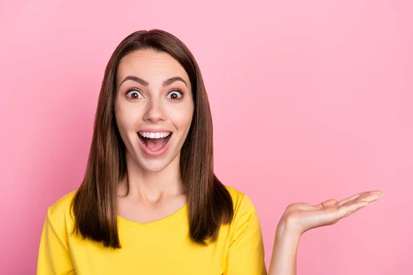 Bild av imponerad brunett hår ung dam hålla handen tomt utrymme bära gul t-shirt isolerad på rosa färg bakgrund — Stockfoto