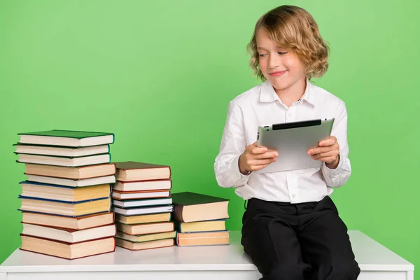 Foto de pequeño niño rubio agradable mantenga la tableta ver libro usar camisa blanca aislada sobre fondo de color verde — Foto de Stock