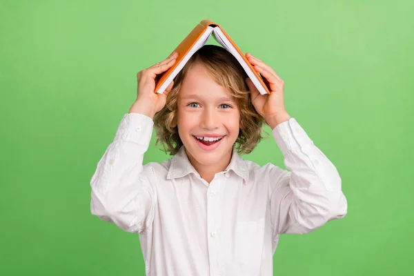 Foto di piccolo divertente ragazzo biondo tenere libro indossare camicia bianca isolata su sfondo di colore verde — Foto Stock