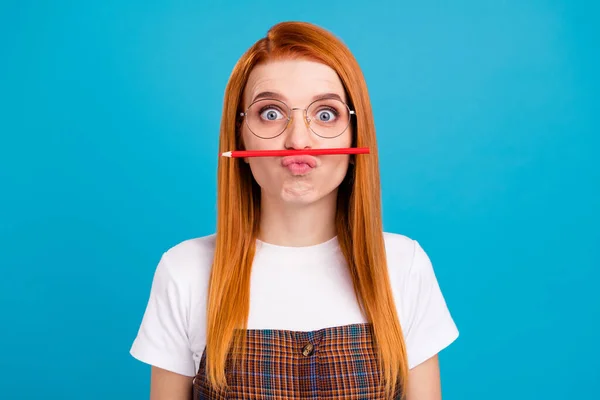 Portrait of attractive funny girl holding pencil on lips like mustache isolated over bright blue color background