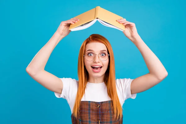 Foto von charmanten aufgeregten orangefarbenen Haaren Dame tragen karierte Gesamtbrille hält Buch wie Dach isoliert blauen Farbhintergrund — Stockfoto