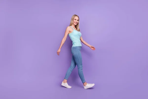 Full body profiel foto van mooie blonde jonge dame ga dragen teal top jeans sneakers geïsoleerd op violette kleur achtergrond — Stockfoto