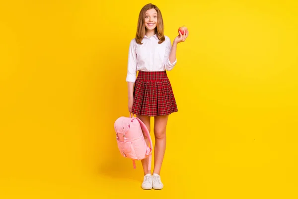 Teljes hosszúságú fotó édes kislány hold alma viselet ing szoknya táska tornacipő elszigetelt sárga háttér — Stock Fotó