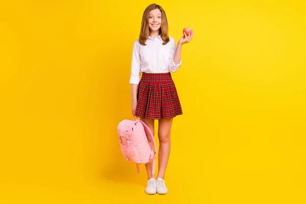 Foto de longitud completa de la niña pequeña dulce mantenga las zapatillas de deporte de la falda de la camisa del desgaste de manzana aisladas sobre fondo amarillo — Foto de Stock