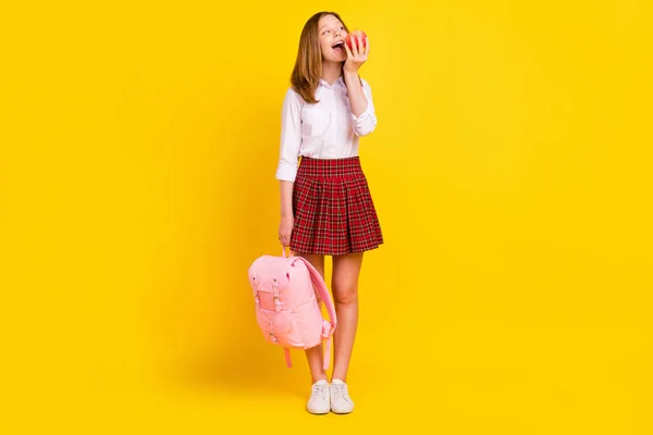 Foto de cuerpo completo de niña agradable comer manzana desgaste camisa falda bolso zapatillas aisladas sobre fondo amarillo —  Fotos de Stock