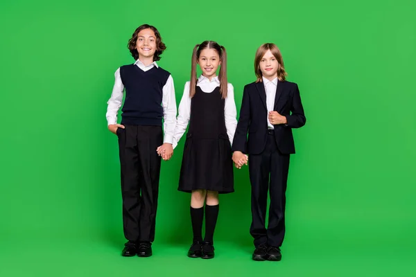 Foto de longitud completa de los niños lindos niña toman de la mano usan uniforme de la escuela aislado sobre fondo verde — Foto de Stock