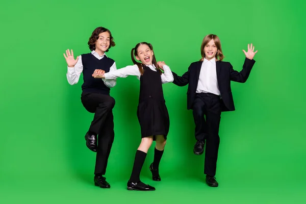 Corpo inteiro foto de impressionado menina meninos segurar as mãos ir onda desgaste escola uniforme isolado no fundo verde — Fotografia de Stock