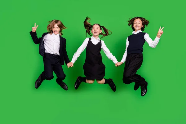 Foto de cuerpo completo de los niños hooray niña salto v-signo de usar zapatos de uniforme de la escuela aislados sobre fondo verde — Foto de Stock