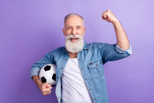 Фото пожилого человека счастливой позитивной улыбкой держать футбольный мяч радоваться победе кулаки руки изолированы на фиолетовом фоне цвета — стоковое фото