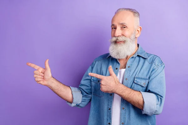 Photo of cheerful positive age gentleman wear jeans shirt pointing two fingers empty space isolated violet color background — Stockfoto