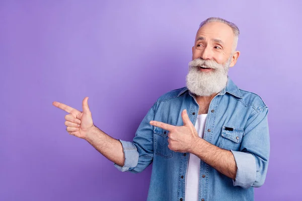 Photo of cute charming mature man dressed denim outfit looking pointing finger empty space isolated purple color background — Stockfoto