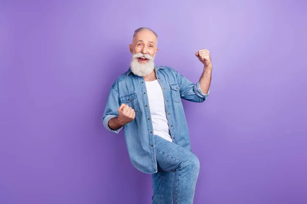 Photo of confident lucky mature man dressed denim outfit smiling rising fists isolated purple color background —  Fotos de Stock