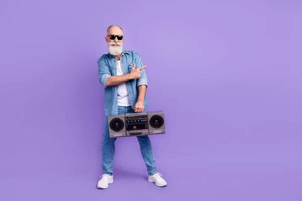 Full body foto van oude man gelukkig positieve glimlach houden boombox punt vinger leeg ruimte advertentie keuze geïsoleerd over paarse kleur achtergrond — Stockfoto