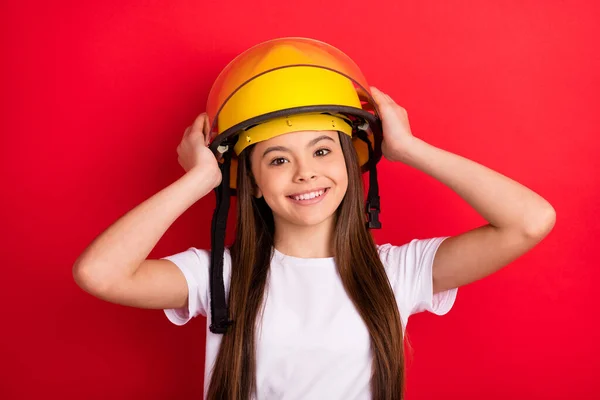 Foto van jong meisje gelukkig positieve glimlach handen aanraken helm brandweerman geïsoleerd over rode kleur achtergrond — Stockfoto