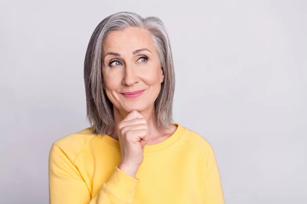 Photo of sweet thoughtful age woman dressed yellow outfit smiling arm chin looking empty space isolated grey color background — Stockfoto