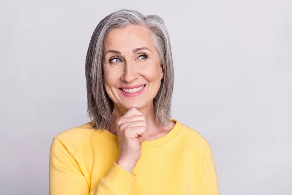 Photo of cute dreamy mature lady wear yellow clothes arm chin looking empty space smiling isolated grey color background — Stockfoto