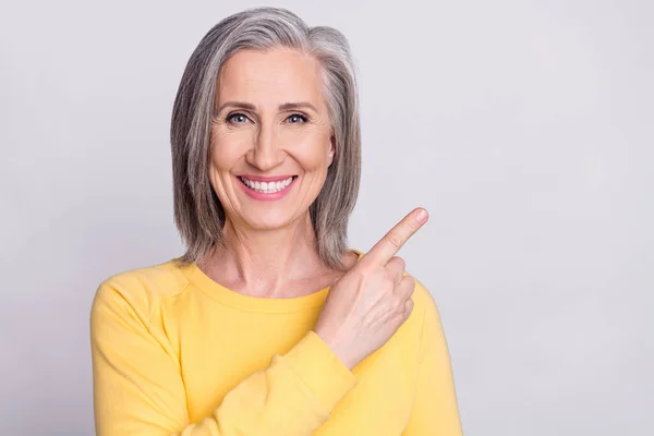 Photo of dreamy sweet mature lady wear yellow clothes pointing finger empty space smiling isolated grey color background — Fotografia de Stock