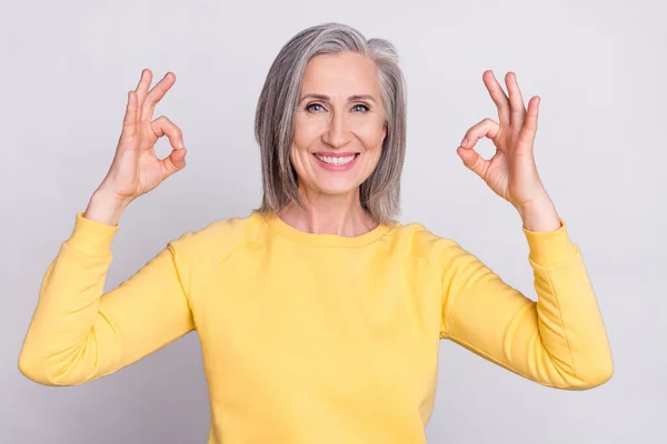 Photo of happy cheerful good mood mature woman showing okay sign wear yellow sweater isolated on grey color background — Fotografia de Stock