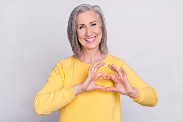 Photo of happy cheerful smiling positive mature woman showing heart shape sign isolated on grey color background — Fotografia de Stock