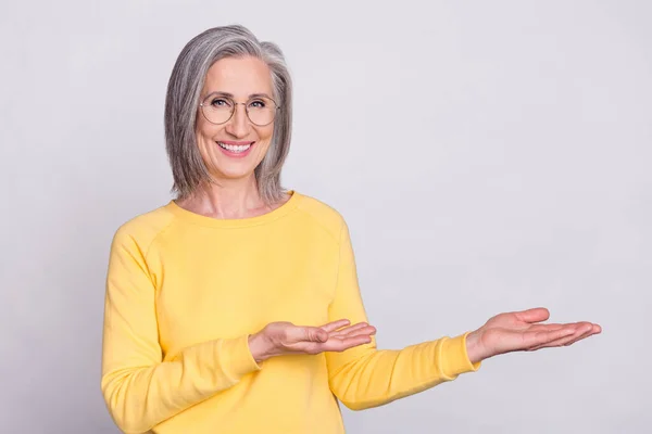 Photo of happy cheerful smiling lovely mature woman in glasses recommending product isolated on grey color background — Φωτογραφία Αρχείου