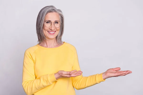 Photo of happy cheerful smiling lovely mature woman in glasses recommending product isolated on grey color background — Fotografia de Stock