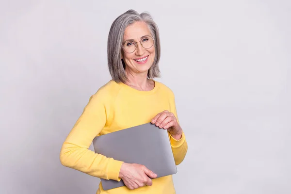 Foto van gelukkig goed humeur vrolijke volwassen vrouw in bril houden laptop dragen gele trui geïsoleerd op grijze kleur achtergrond — Stockfoto