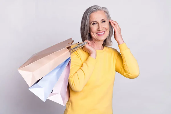 Photo of beautiful charming positive smiling mature woman hold bags after shopping isolated on grey color background — Photo