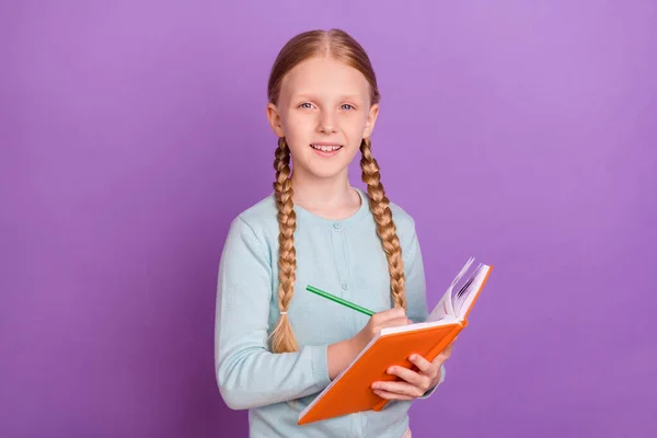 Foto van positieve pupil meisje houden notebook schrijven huiswerk dragen blauw shirt geïsoleerde violette kleur achtergrond — Stockfoto