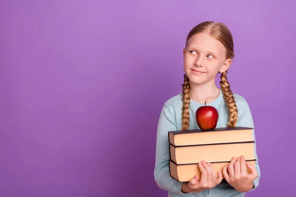 Photo of curious smart learner girl hold book apple look empty space wear blue shirt isolated violet color background — Stock Photo, Image