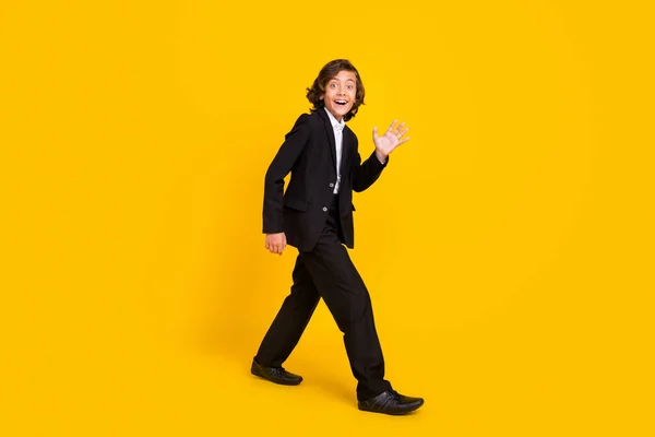 照片上，友善而兴奋的小男孩走着挥手，穿着黑色制服鞋，背景是孤立的黄色 — 图库照片