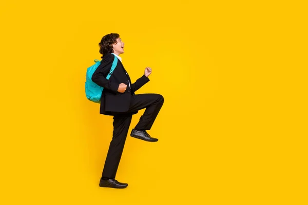 Profilfoto von Champion triumphierenden kleinen Schuljungen tragen Rucksack schwarze Uniform isoliert gelbe Farbe Hintergrund — Stockfoto